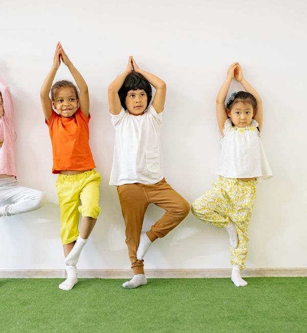 A diverse group of kids stretching together on colorful yoga mats in a sunlit room.