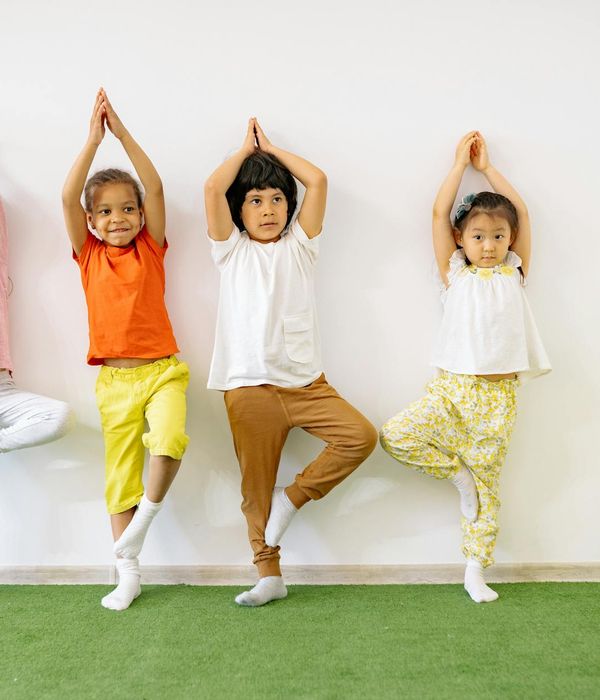 Group of happy children doing a simple yoga pose in a bright, colorful room.